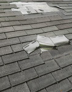 Asphalt shingles of a roof are damaged and laying on the roof.