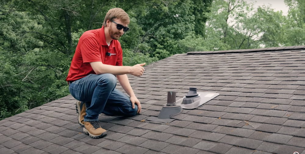 A roofer is kneeling on a roof and explains roofing issues.